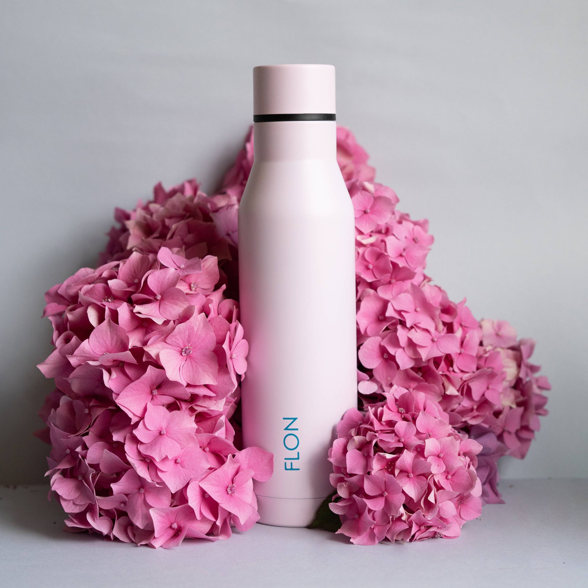 White water bottle with pink cap surrounded by pink flowers on a light gray background