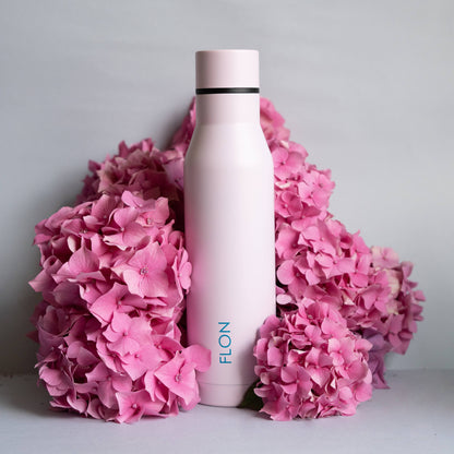 White water bottle with pink cap surrounded by pink flowers on a light gray background