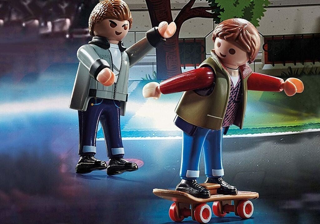Playmobil figures of two characters, one on a skateboard, against a blurred urban background.