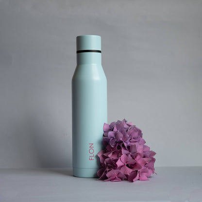 Light blue water bottle with 'FLO' branding next to pink flowers on a gray background