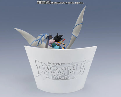 Dragon Ball Z Daima figure display stand featuring Goku and Vegeta in a cup-like base with Dragon Ball Z Daima branding, shown on a blue-gray gradient background.